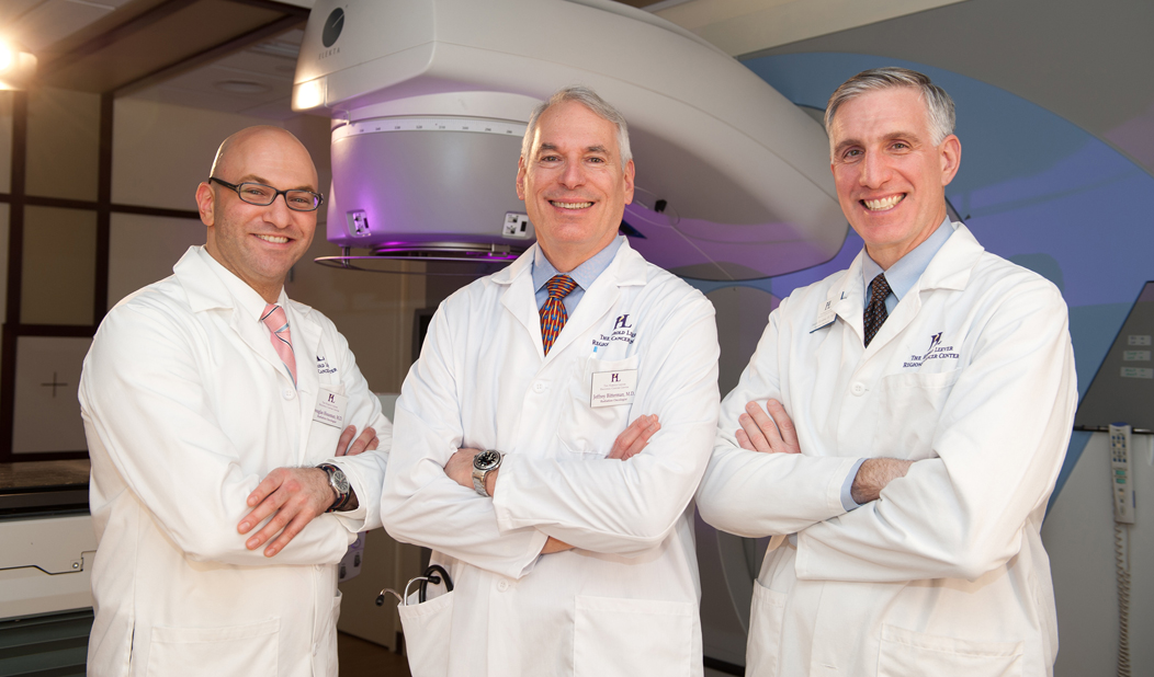 Three male doctors in white coats smiling and standing with arms crossed in the Harold Leever Regional Cancer Center in Waterbury