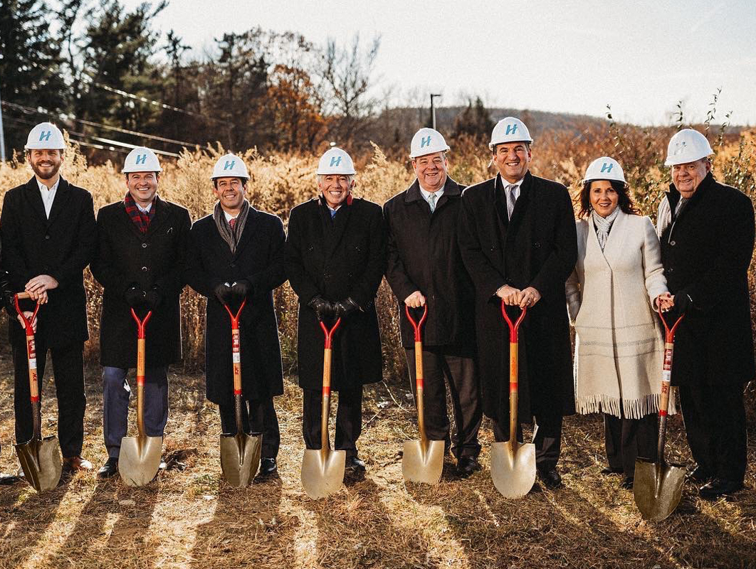 8 members of the Hoffman BMW team wearing white branded hard hats and holding shovels