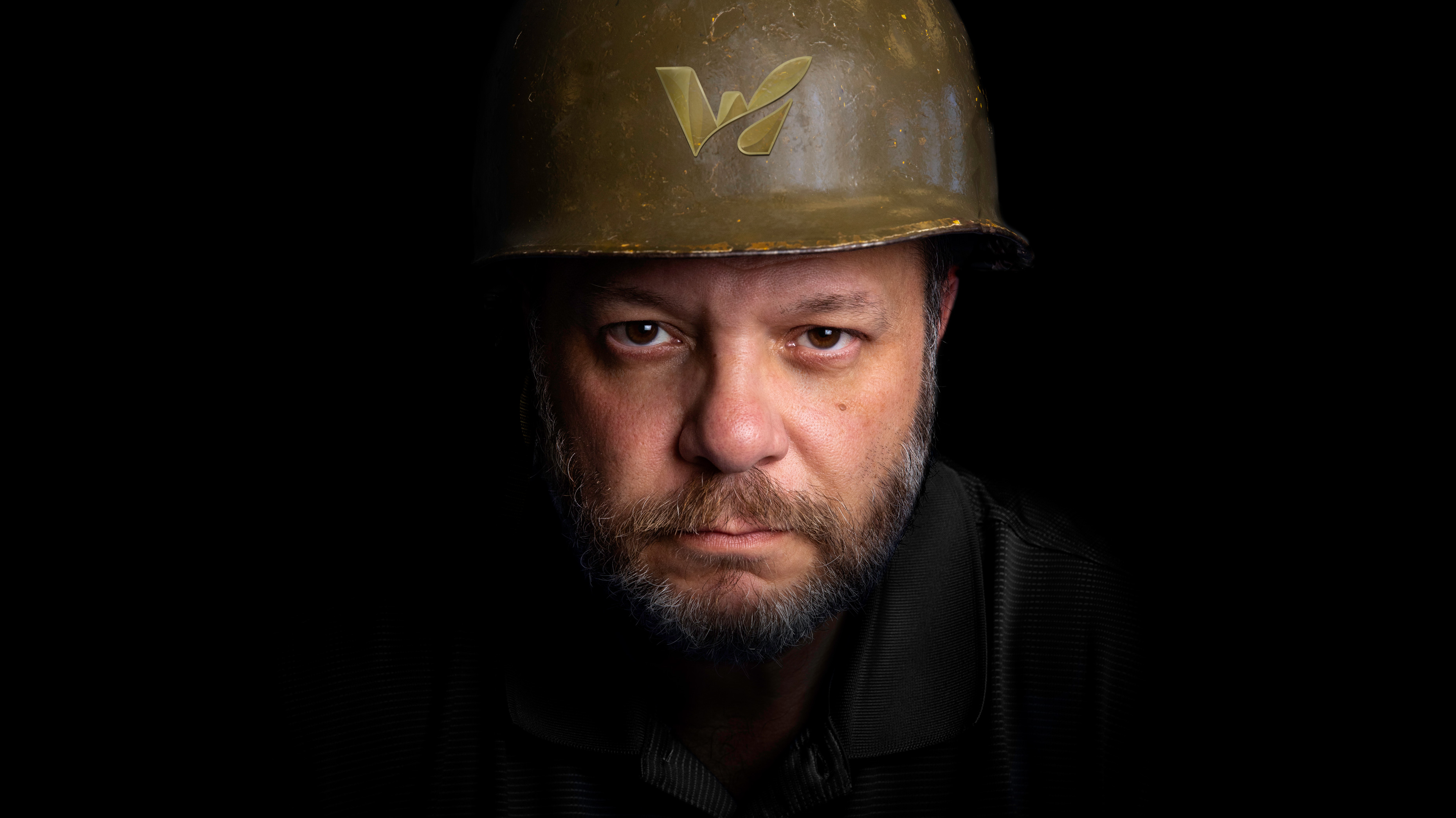 A close up headshot of Frank Monteiro wearing an army helmet with The Waterbury logo