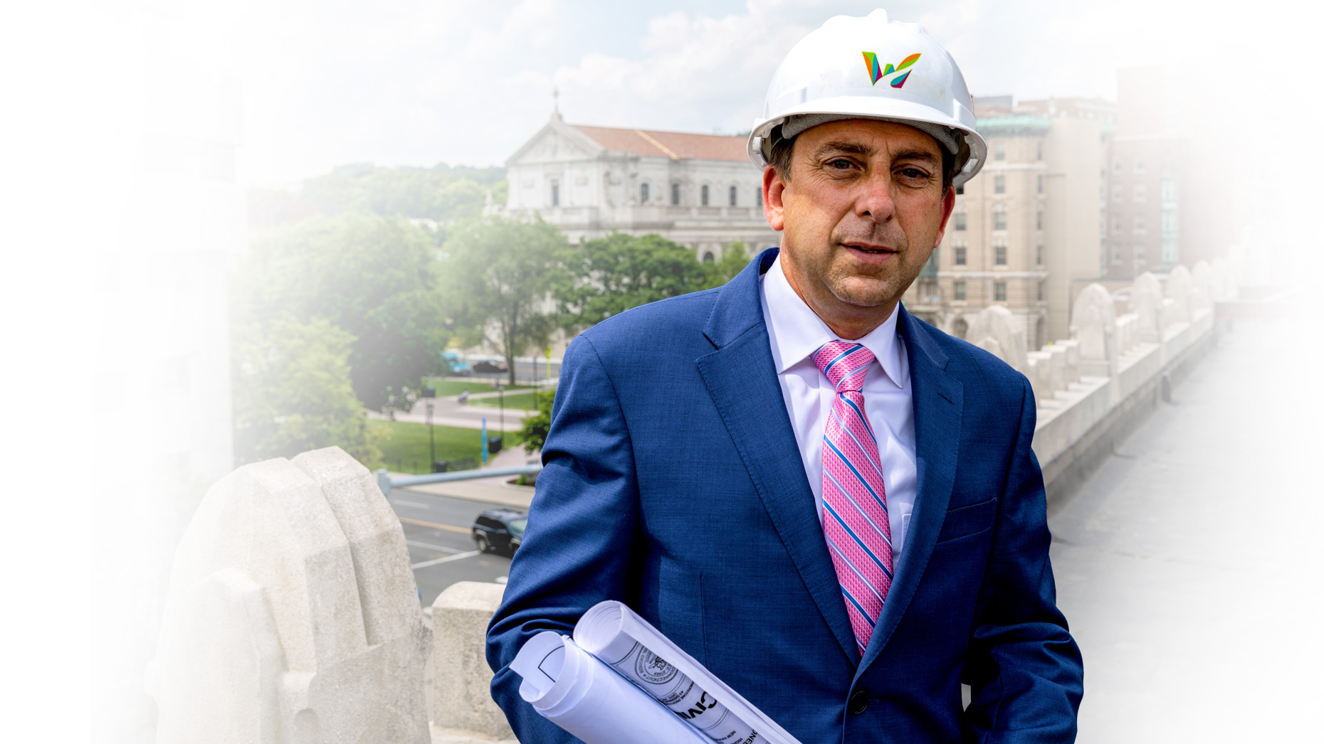 Joe Gramando wearing a Waterbury hard hat and holding blueprints, standing by the Waterbury Green