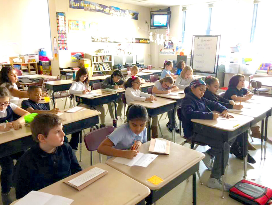Young Waterbury CT school students sitting at their desks in a classroom completing an assignment