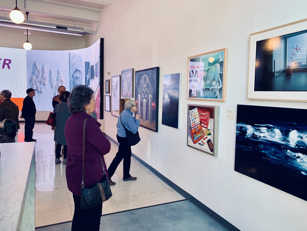 Patrons viewing framed artwork on the walls at Post University art gallery exhibit in Waterbury CT