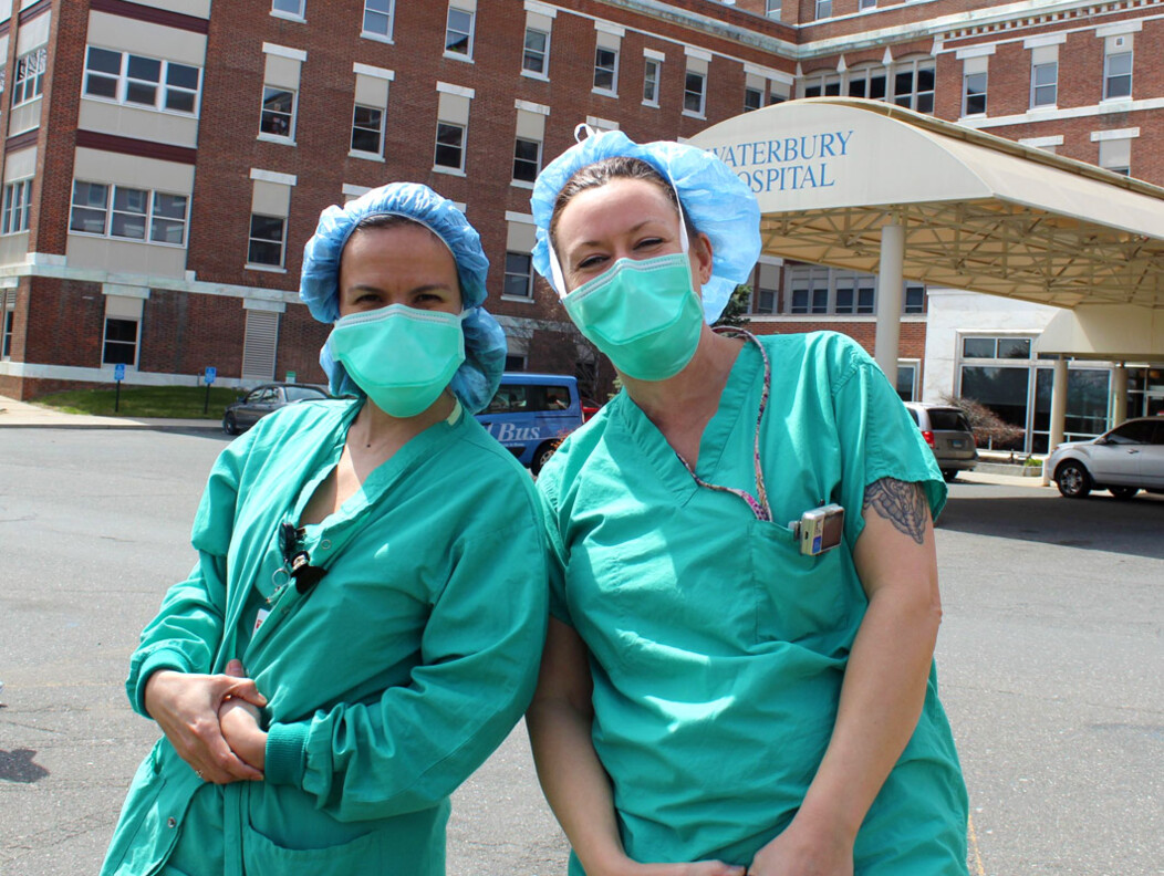 Two female members of the Waterbury Hospital team wearing hair covers and face masks standing outside the hospital