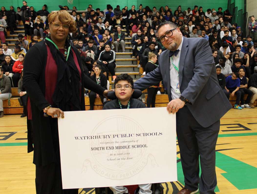 Waterbury student in wheelchair between and man and woman standing in front of student audience