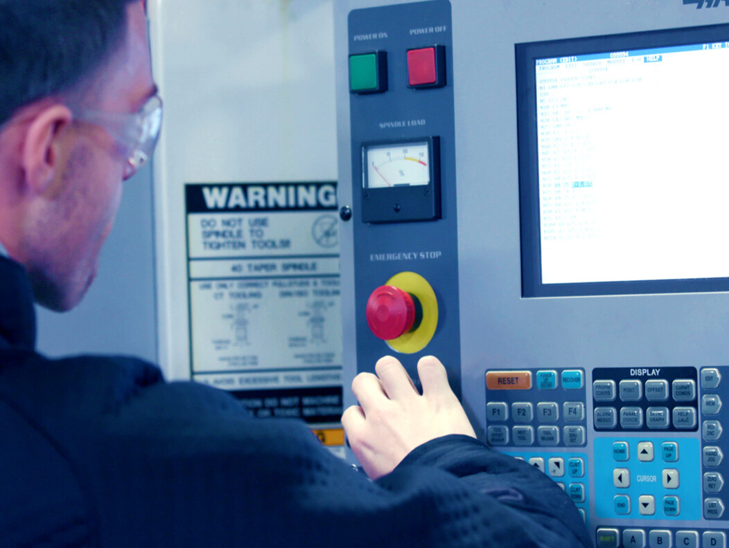 Man wearing protective goggles looking at the screen on a large machine and preparing to push a large red button