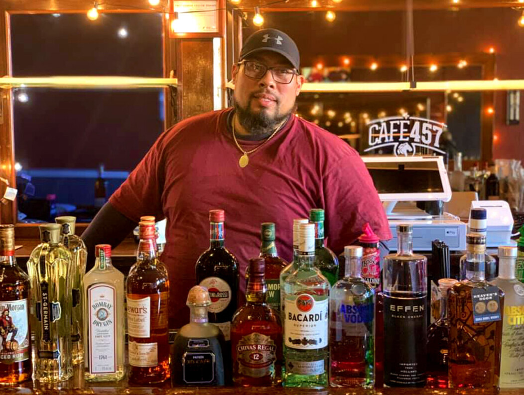 Man standing behind a bar filled with various liquor bottles at Cafe 457 in Waterbury CT